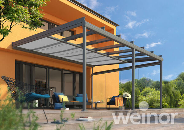 Moderne Terrassenüberdachung aus Glas an einem Einfamilienhaus mit Gartenmöbeln.