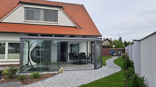 Modernes Einfamilienhaus mit Wintergarten und gepflegtem Gartenweg im Grünen.