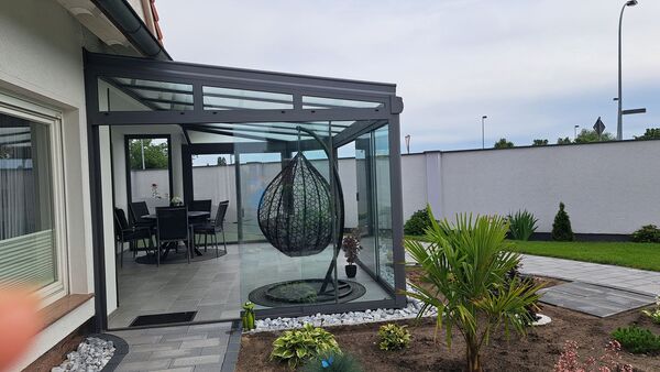 Moderner Wintergarten mit Glasüberdachung, Hängesessel und gepflegtem Gartenbereich.