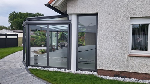 Moderner Wintergarten mit Glasfront und Sichtschutzfolie an Einfamilienhaus im Garten.