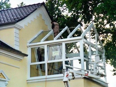 Ein Bauarbeiter montiert ein Glasdach für einen Wintergarten an einem gelben Haus.