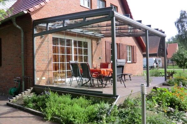 Moderne Terrassenüberdachung aus Glas an einem Einfamilienhaus mit Gartenmöbeln.