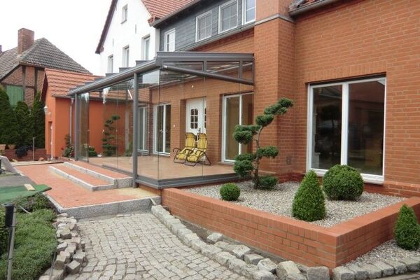Moderner Wintergarten aus Glas mit Metallrahmen an einem roten Klinkerhaus und Steingarten.