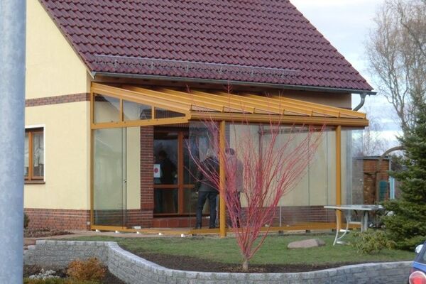 Moderner Wintergarten mit Glaswänden an Einfamilienhaus mit rotem Ziegeldach und Garten.