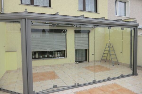 Moderne Terrassenüberdachung aus Glas mit Aluminiumrahmen an einem Einfamilienhaus.