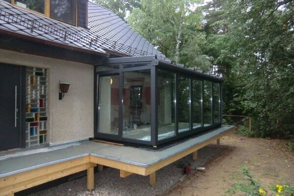 Moderner Wintergarten aus Glas mit Aluminiumrahmen an einem Einfamilienhaus im Grünen.