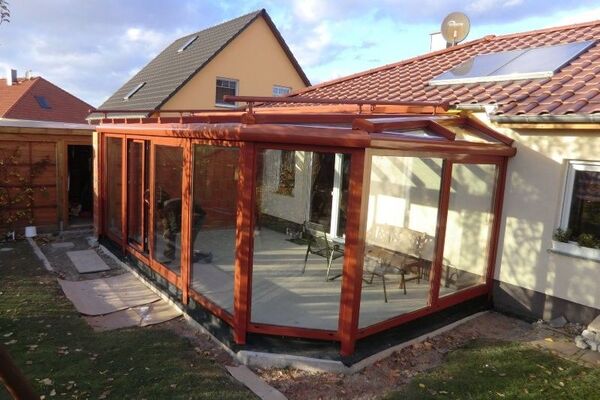 Moderner Wintergarten aus Glas mit Holzrahmen an Einfamilienhaus im Garten Bereich.