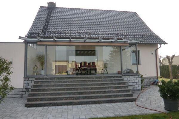 Modernes Einfamilienhaus mit großer Glas-Terrasse und gepflastertem Eingangsbereich.