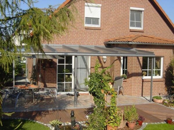 Überdachte Terrasse mit Glasdach an einem roten Einfamilienhaus mit Garten und Gartenmöbeln.