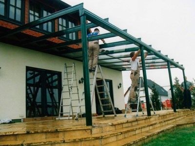 Handwerker montieren ein Terrassendach aus Glas und Metall an einem Einfamilienhaus.