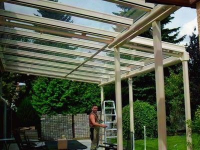 Handwerker baut ein Terrassendach aus Glas im Garten bei sonnigem Wetter auf.