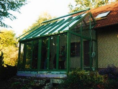 Moderner Wintergarten mit Glasdach und grünem Metallrahmen an einem Einfamilienhaus