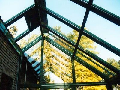 Modernes Glasdach eines Wintergartens mit Ausblick auf Bäume und blauem Himmel.